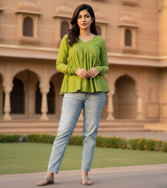 Woman wearing a green top and light blue jeans standing in front of an architectural building.